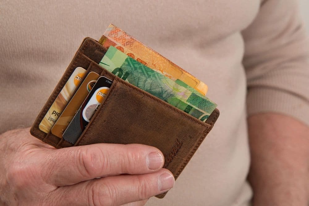 A hand holding a leather wallet with cash and cards