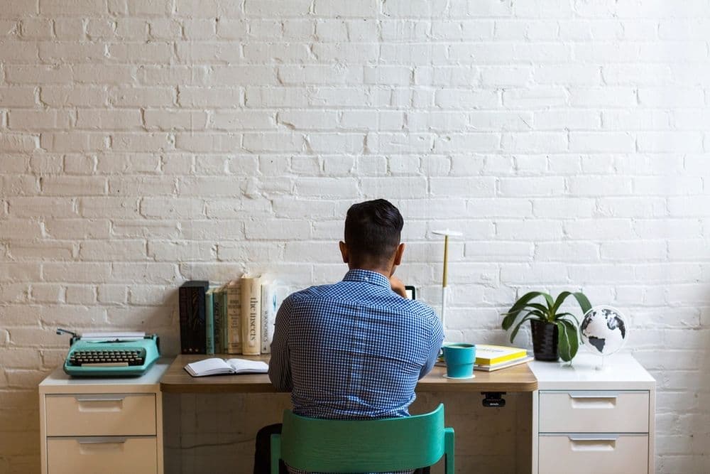 A person working at a desk against a white brick wall