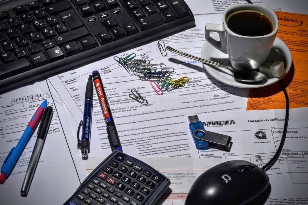Invoices, pens, a calculator and coffee on an office desk